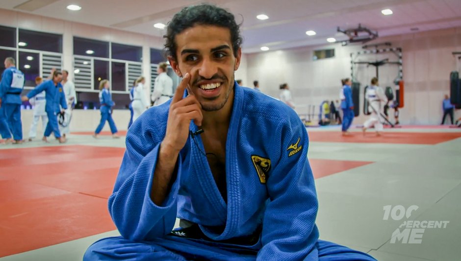 Shugaa Naswan Portfolio: Shugaa im blauen Judo-Anzug, auf der Matte sitzend, erzählt Anekdoten aus dem Judo-Alltag